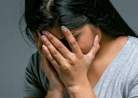 A woman hides her face in hands showing deep emotion and sadness in a studio setting.