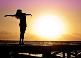 A joyful silhouette of a woman standing on a dock at sunset, embracing the freedom of nature.